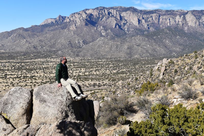 a hiker rests on a rocky bluff staring at desert mountains in the background