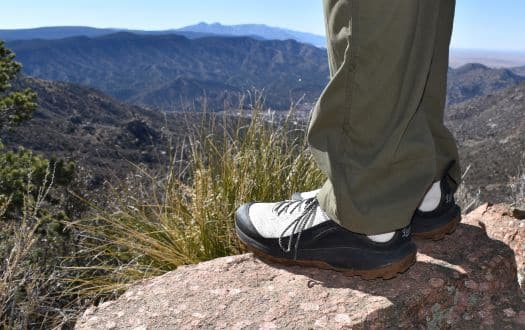 a hiking shoe in the foreground with blurred mountains in the background 