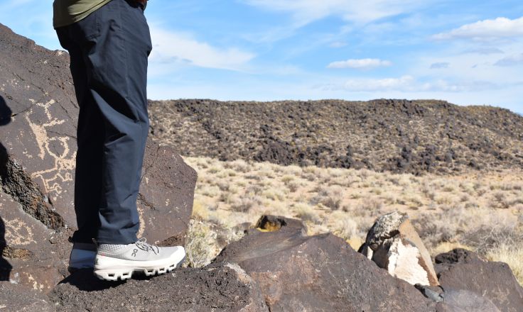 Hiker stands on boulders looking out on a desert landscape